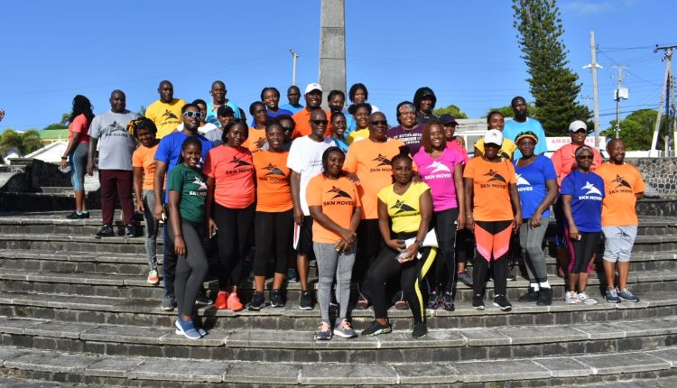 Prime Minister Dr the Hon Timothy Harris, Minister of Health the Hon Akilah Byron-Nisbett, and Deputy Speaker Senator the Hon Dr Bernicia Nisbett, pose for a group picture at the end of the walk with a subset of participants at the Cenotaph.