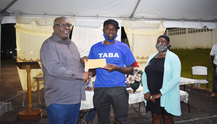 Deputy Captain of Tabernacle Domino Club Mr Kerone Roache receives a cheque of $5,000 from league sponsor Prime Minister Harris. Looking on is Ms Sandra Duggins who assisted with the distribution of prizes.