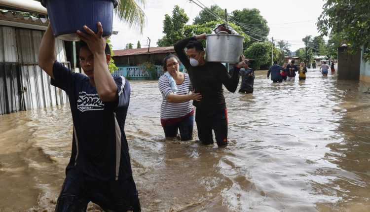 Residents wade through floodwaters carrying their belongings in the neighborhood of Suyapa, Honduras, Thursday, Nov. 5, 2020. The storm that hit Nicaragua as a Category 4 hurricane on Tuesday had become more of a vast tropical rainstorm, but it was advancing so slowly and dumping so much rain that much of Central America remained on high alert. (AP Photo/Delmer Martinez)