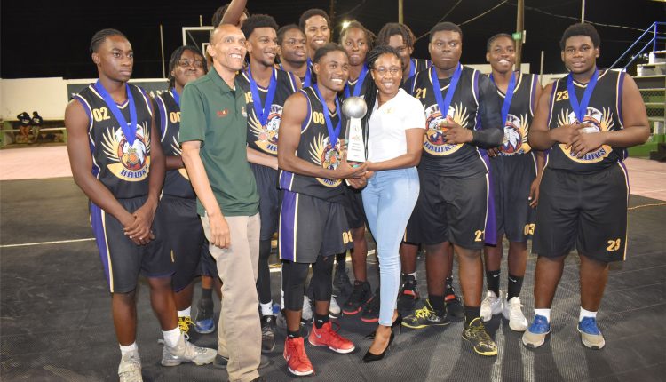 Ms Chantelle Rochester presents the Development Bank of St. Kitts and Nevis Junior Division Under-20 Basketball championship trophy to Aaron Wilkinson as ASC Jay Hawks players cheer on. With them is SKABA President, Glenville Jeffers.